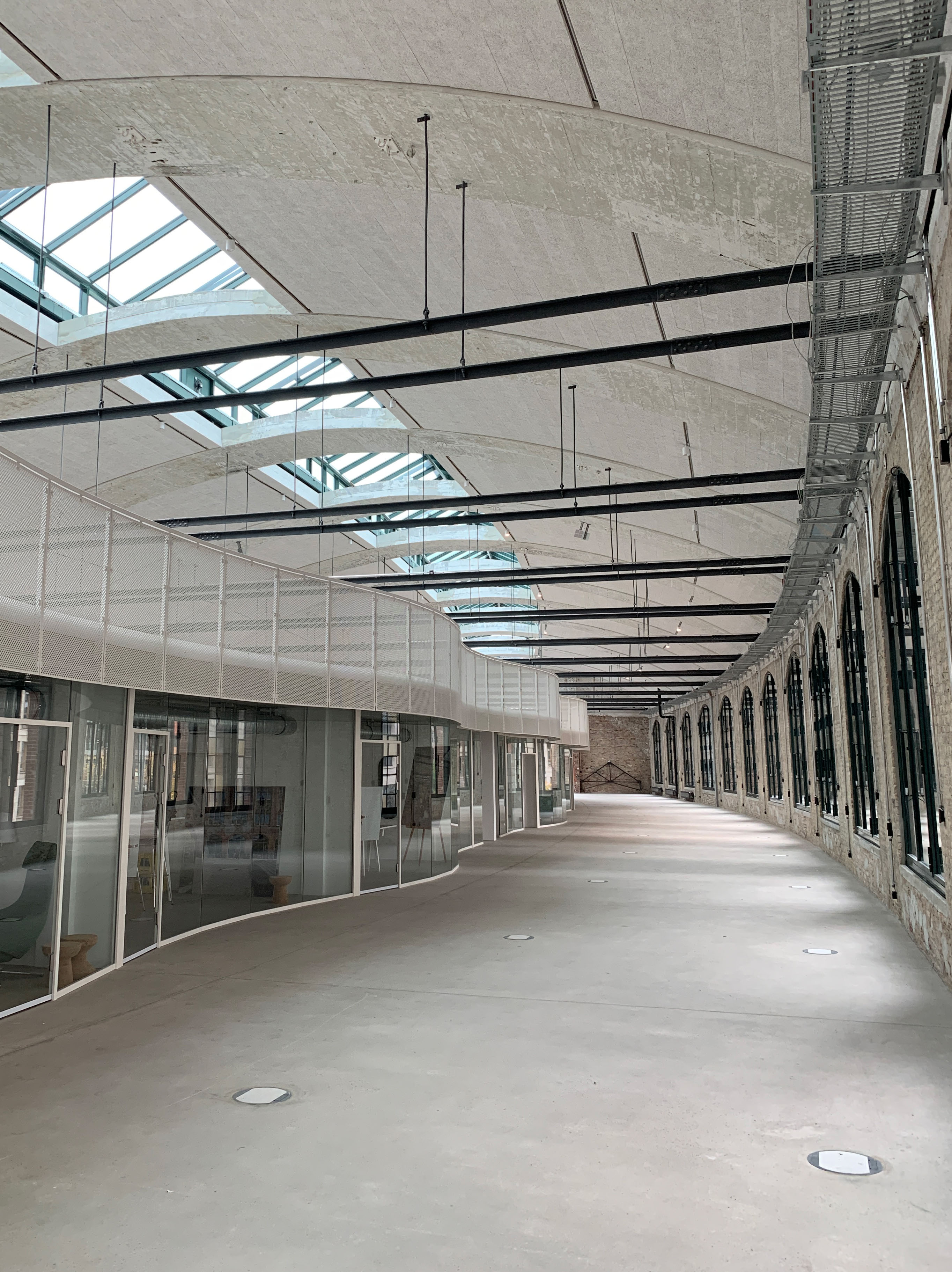 Großer lichtdurchfluteter Flur mit Glasfassaden und abgehängter Decke, Blick entlang der geschwungenen Architektur.