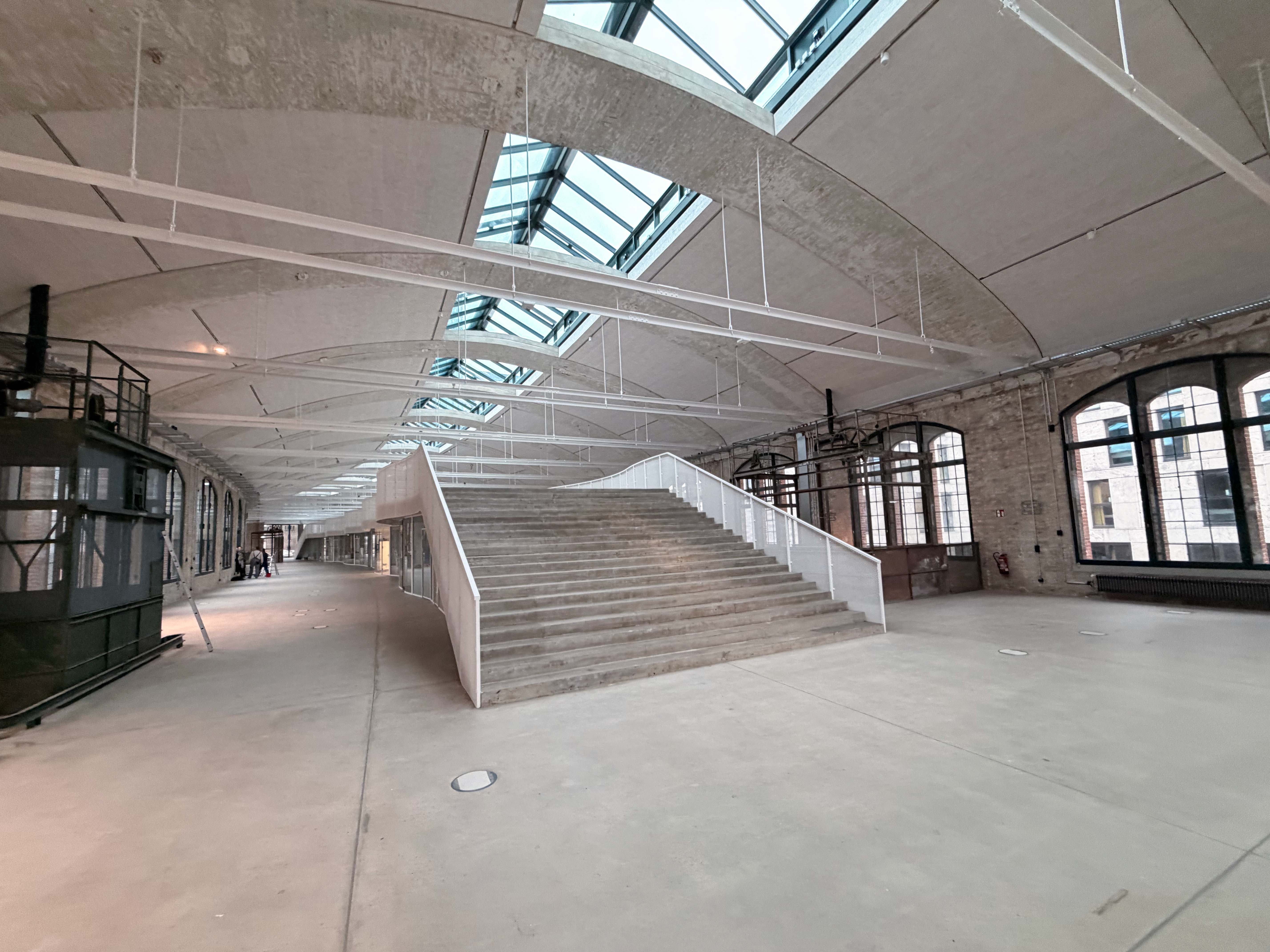 Der Baufortschritt im Postbahnhof Berlin zeigt die Eingangspackkammer im 1. OG mit geneigten Ebenen, Oberlichtern und einer offenen Raumgestaltung.