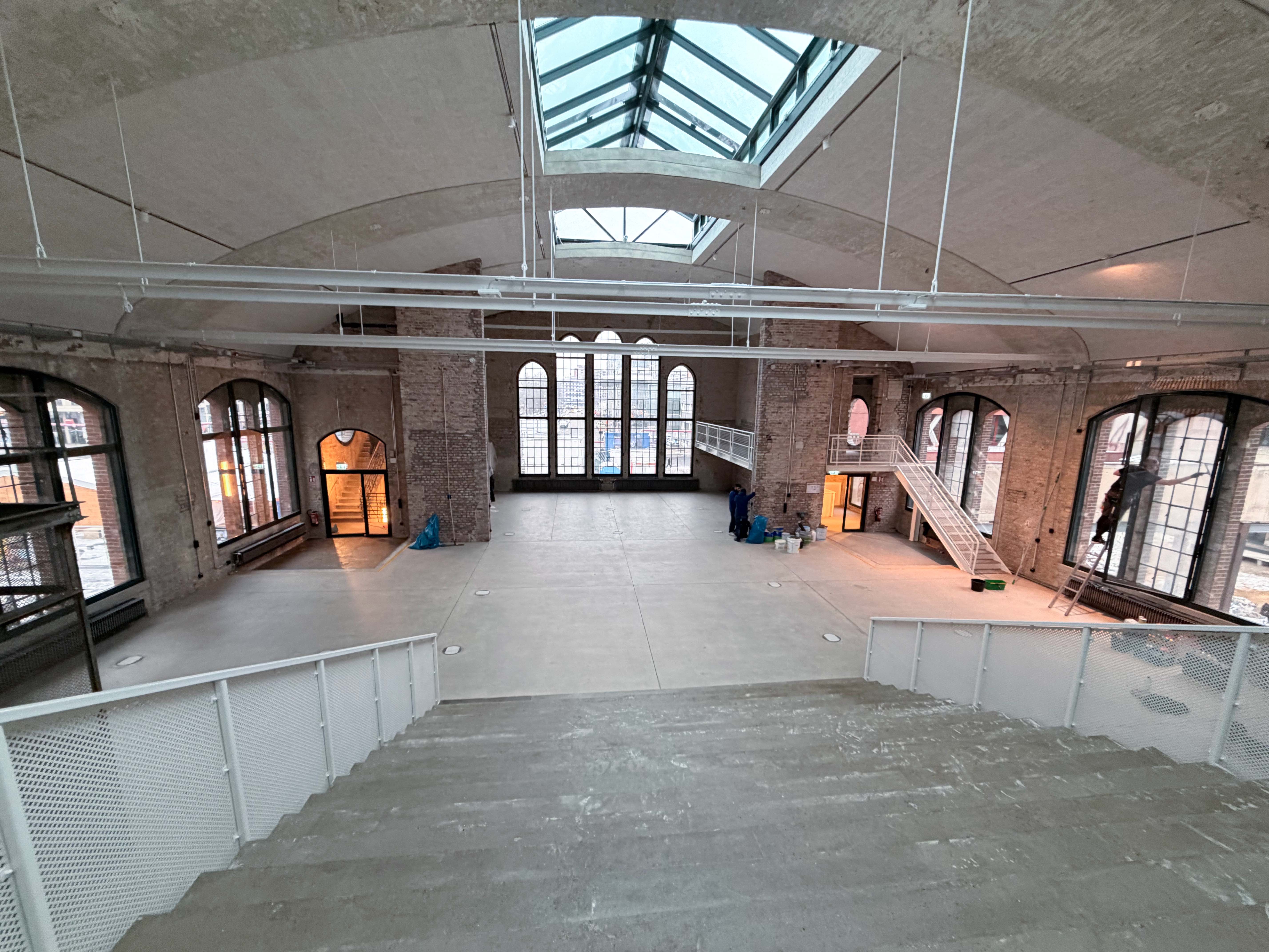 Der Baufortschritt im Postbahnhof Berlin zeigt die Eingangspackkammer im 1. OG mit zentralem Lichthof, umlaufenden Galerien und sichtbaren Deckenstrukturen.