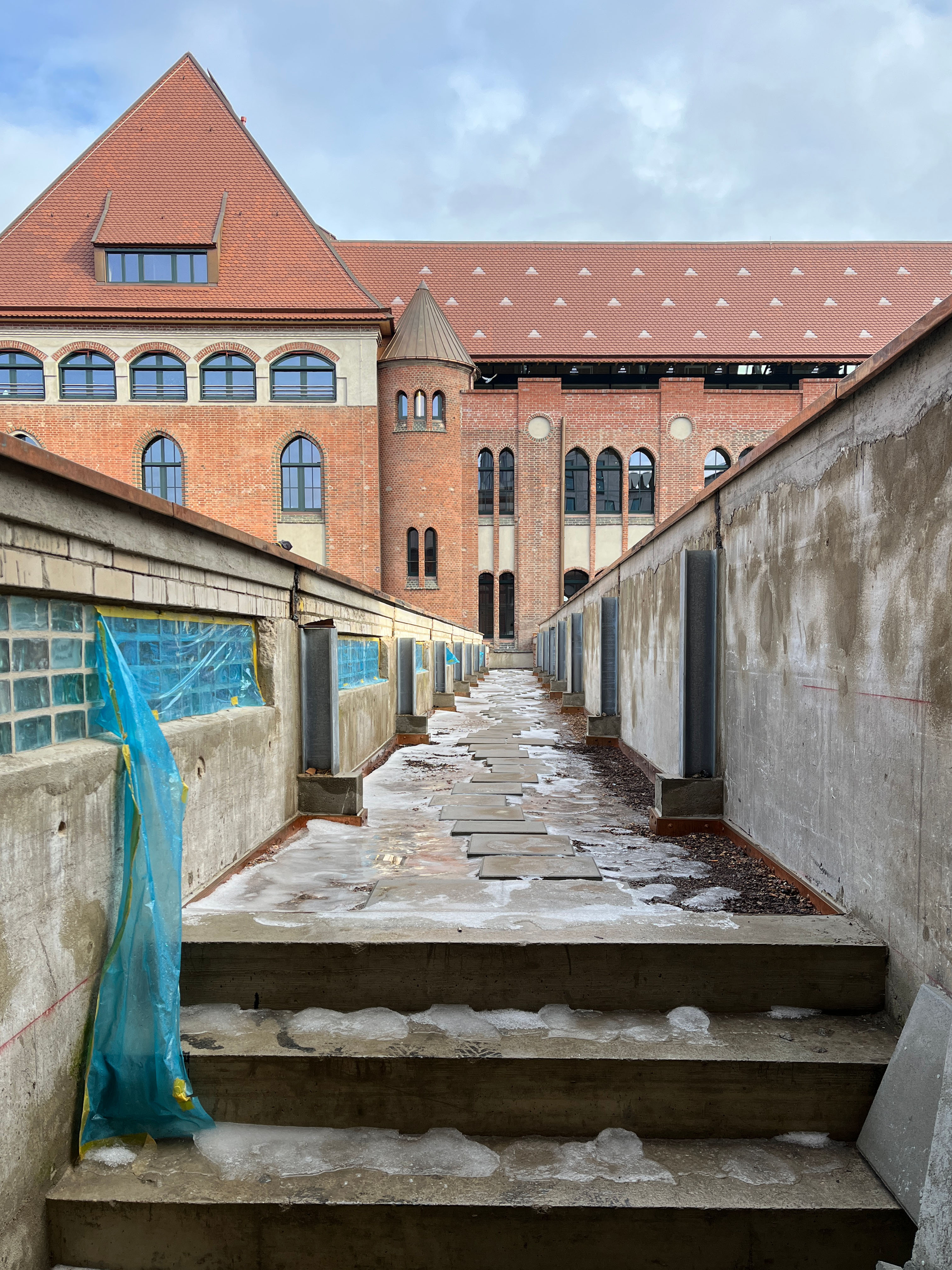 Das Bild zeigt den Baufortschritt im Postbahnhof Berlin mit der Paketband-Terrasse im Außenbereich und Blick auf die historische Backsteinarchitektur.