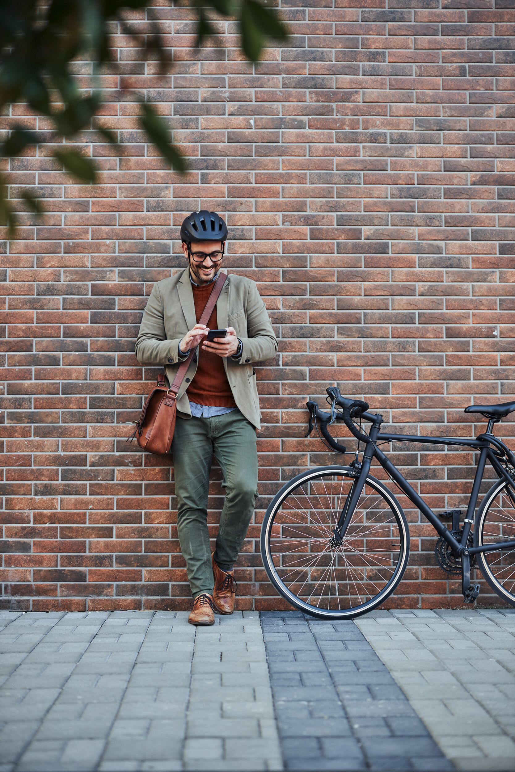 Ein Mann in einem Helm steht an einer Ziegelwand und benutzt sein Smartphone.